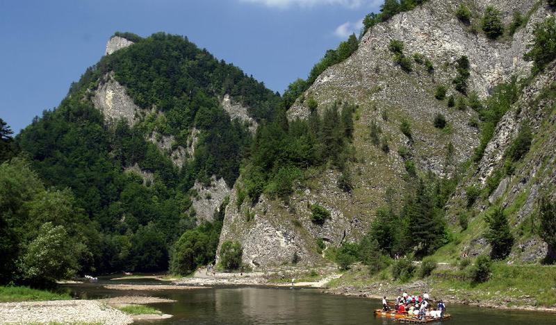 Tratwa pełna ludzi na rzece, wokół rzeki skały.