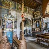 Wnętrze drewnianego kościoła. Boczna ściana nawy z obrazami i ołtarzem oraz przejściem do kaplicy.