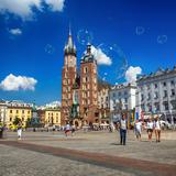 Rynek Główny w Krakowie w słoneczny dzień, w powietrzu unoszą się bańki mydlane, pośrodku zdjęcia Kościół Mariacki