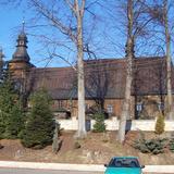 Drewniany kościół z długą nawa i prezbiterium oraz wieżą, widziany z boku.