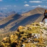 Na szczycie góry siedzi kobieta z plecakiem. Patrzy na panoramę gór przed sobą.