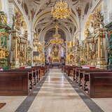 Wnętrze Bazyliki św. Mikołaja w Bochni w jasnej kolorystyce, ołtarze boczne i główny, ławy, złocenia.