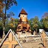 Drewniana, wysoka, bogato zdobiona kaplica na cmentarzu. Przed nią nagrobki w formie drewnianych krzyży.