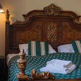 Pokój z dużym, drewnianym łóżkiem, z rzeźbionym zagłówkiem, łóżko przykryte ozdobną, zieloną kapą.
