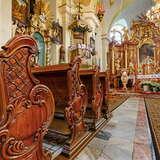 Wnętrze barokowego kościoła z ławkami i ołtarzami.
