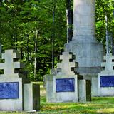 Trzy duże symboliczne betonowe nagrobki z podwójnymi krzyżami. Za nimi część pomnika - kolumny.