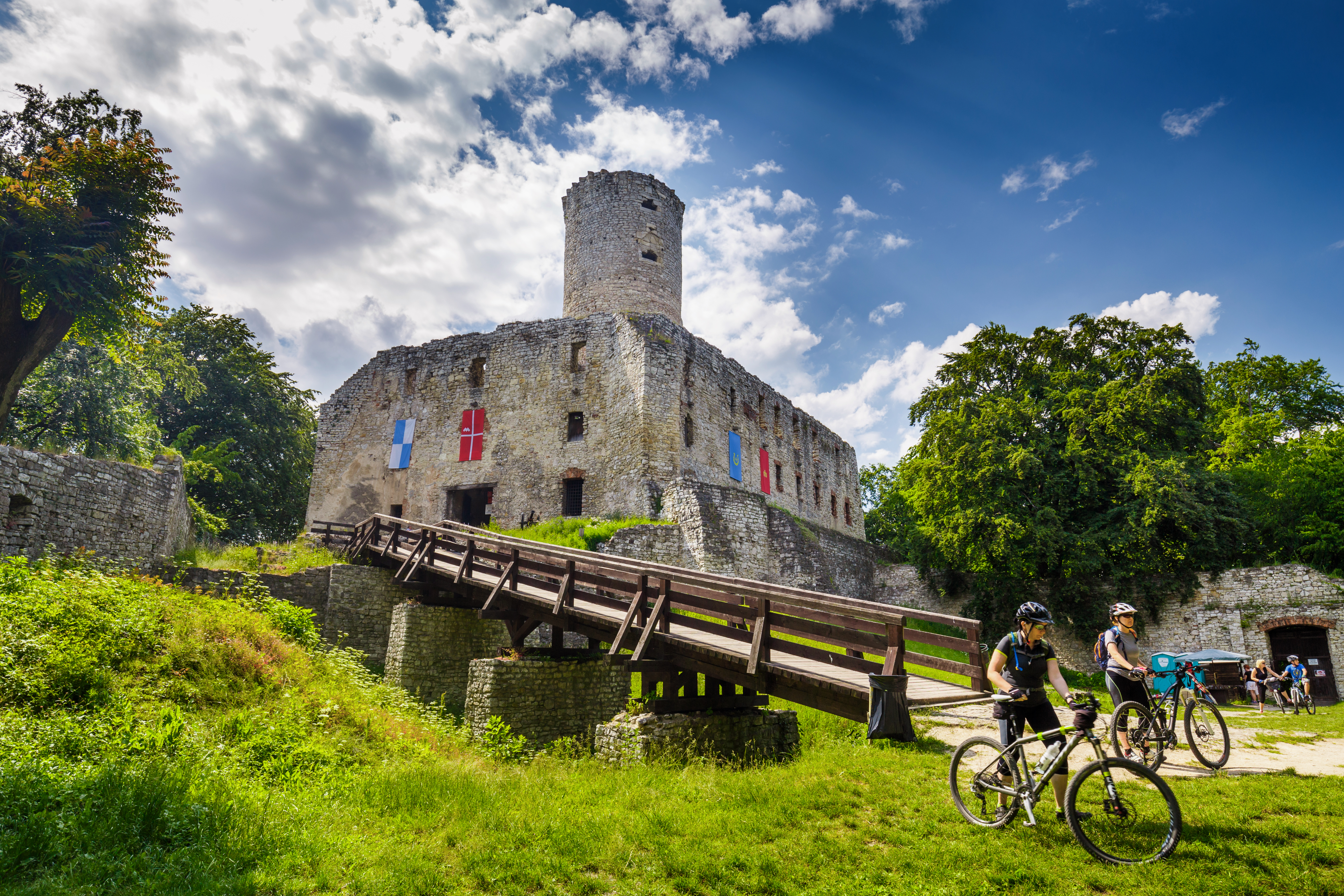 na zdjęciu widać rowerzystów prowadzących rowery pod kamienny zamek 